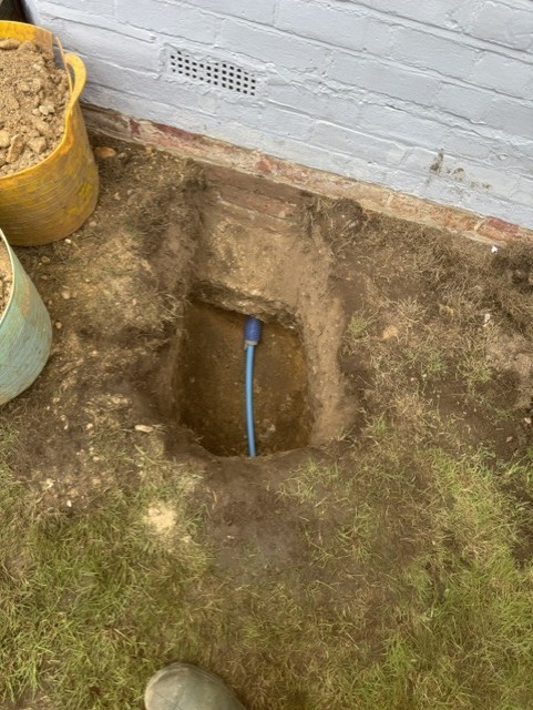 Excavation beside a house wall with a new blue supply pipe