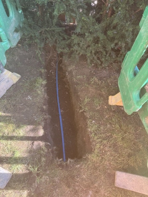 Narrow trench across a lawn with new blue supply pipe laid in it