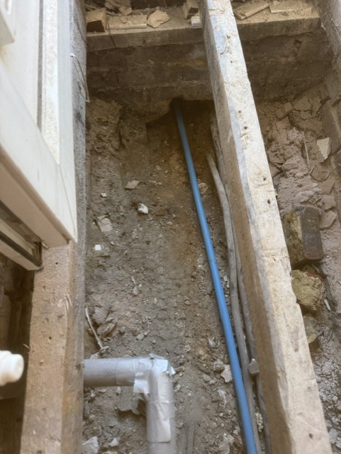 Blue supply pipe laid in a trench along a side passage