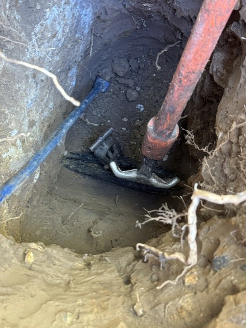 Old red supply pipe and fittings exposed in an excavation