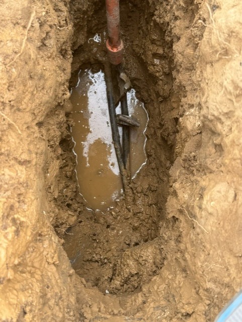 Waterlogged excavation exposing an old supply pipe