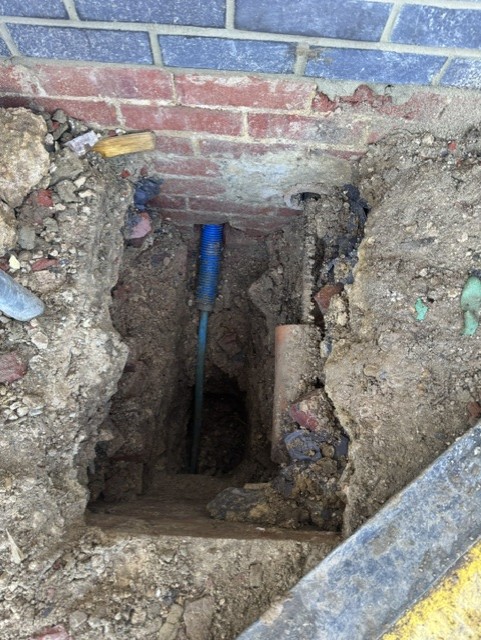 Deep excavation against a brick wall with new blue pipe entering the house