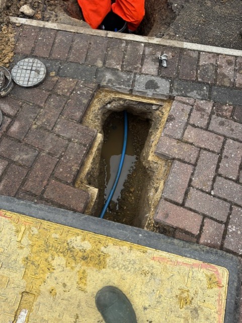 Tidy rectangular excavation in block paving showing blue pipe